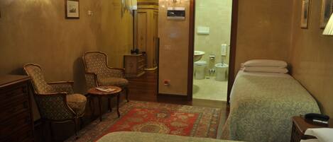 A hotel room with two beds, a sitting area with chairs, a small table, and a bathroom visible through an open door.