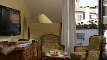 Una habitación con televisor, lámpara, dos sillones, una mesa con cosas para el desayuno y vistas a edificios a través de una ventana.