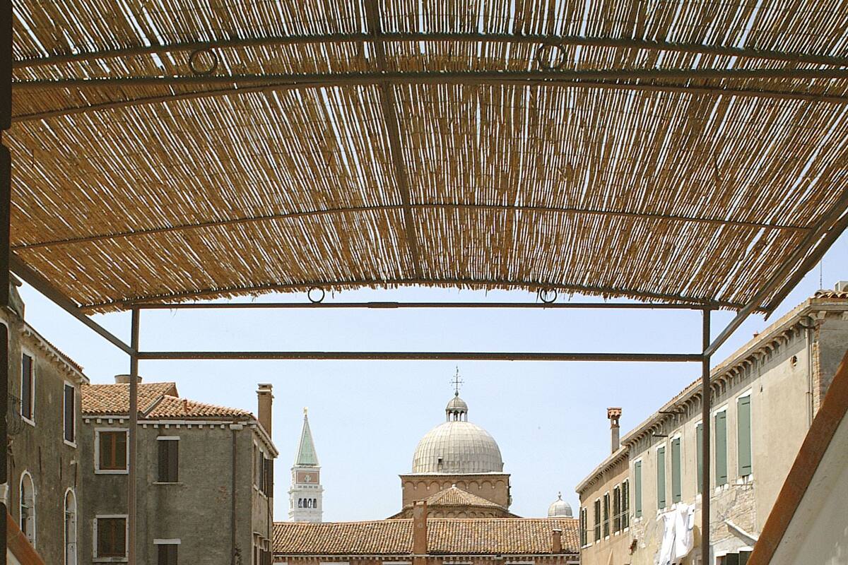 A covered outdoor seating area with a table and chairs, overlooking a historic building with a dome and a tower.