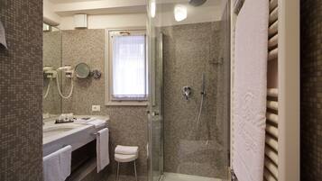 A modern bathroom with a glass-enclosed shower, a vanity with a mirror, and a window with sheer curtains.