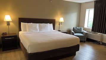 Una habitación de hotel con una cama grande, dos mesitas de noche con lámparas, una silla y un ventanal con cortinas.