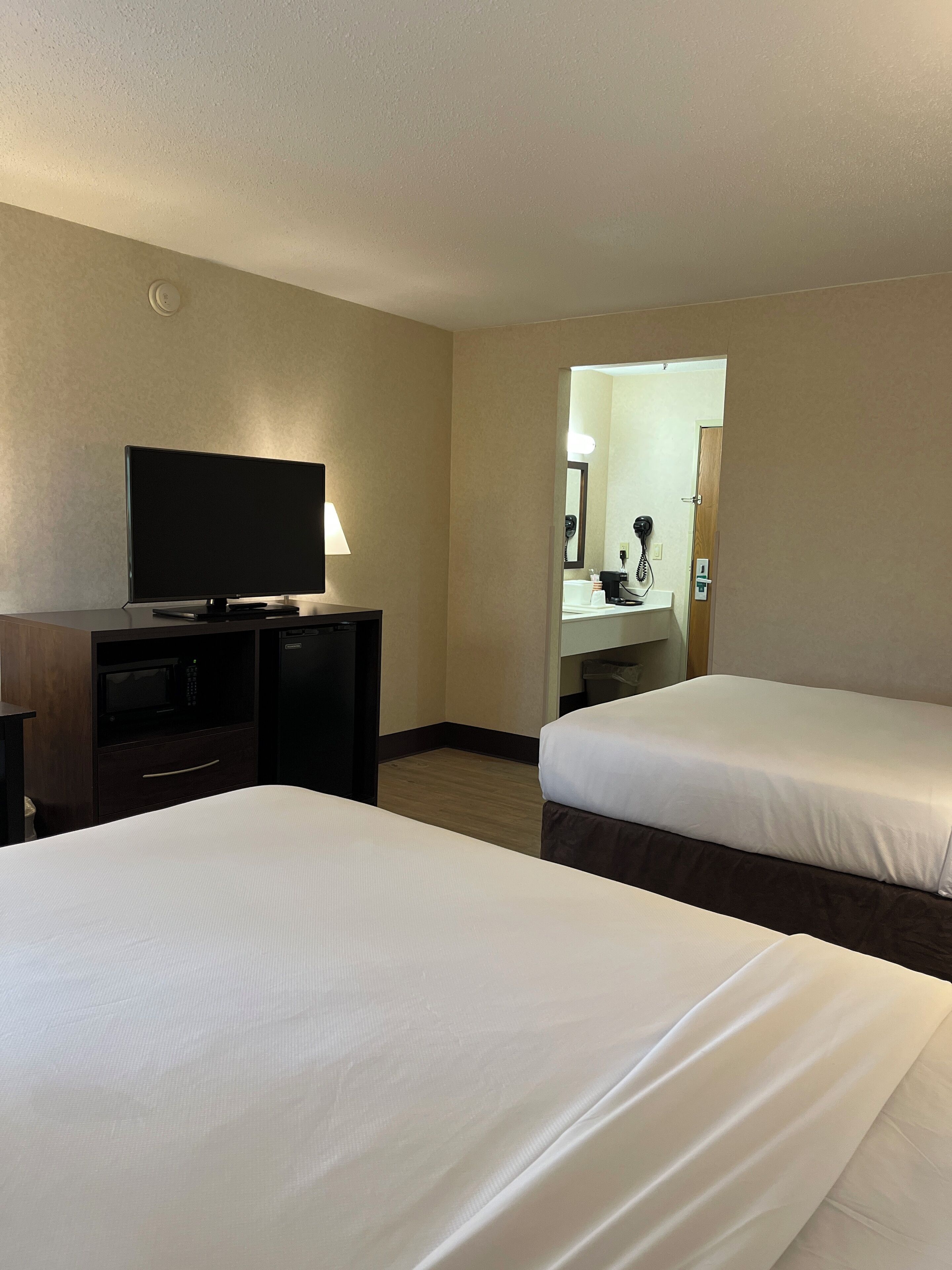 Une chambre d’hôtel avec deux lits, un bureau doté d’un téléviseur à écran plat, un four à micro-ondes et un téléphone.