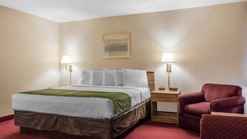 A hotel room with a large bed, two bedside tables with lamps, a red armchair, and a painting on the wall.