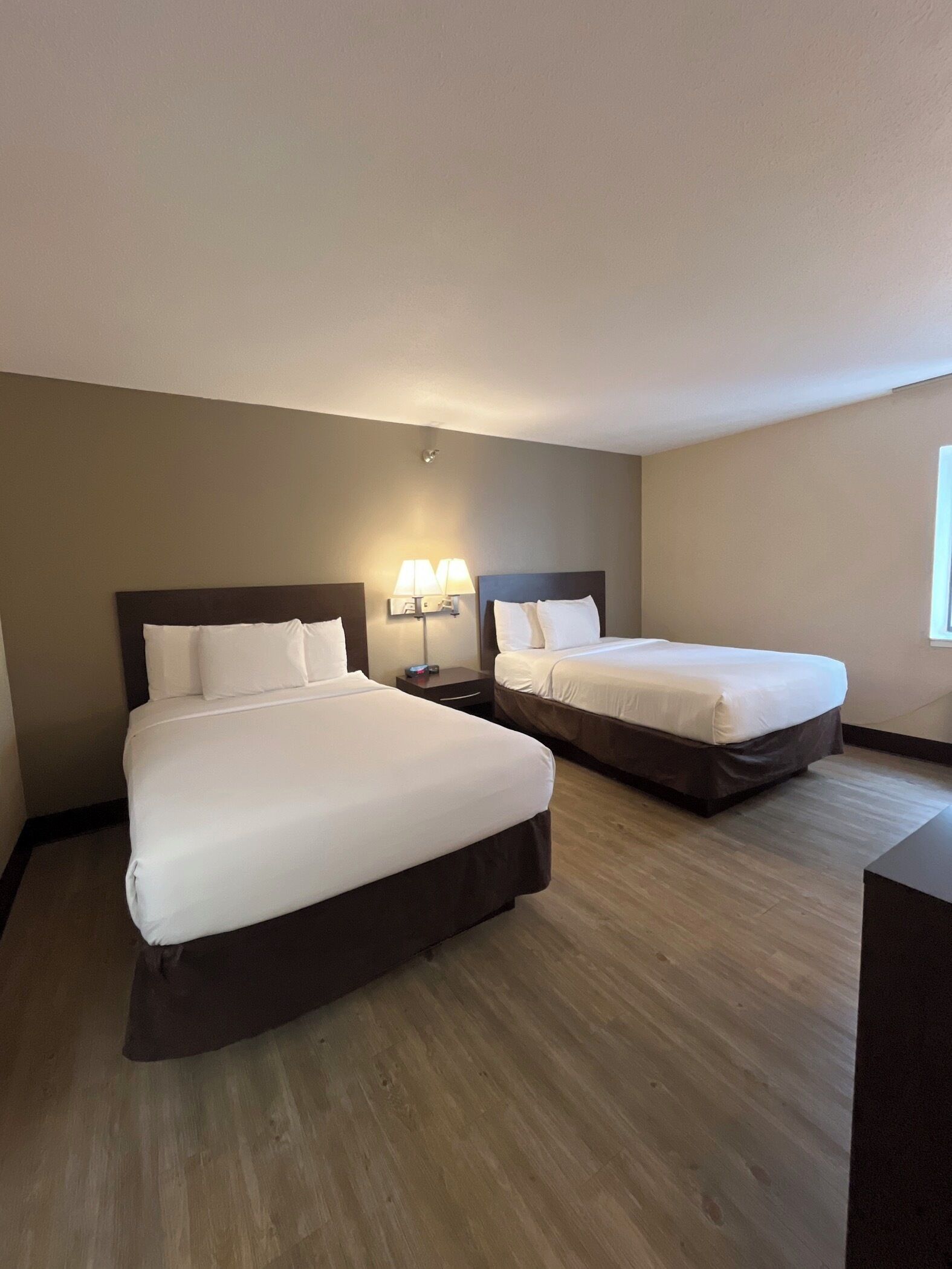 Habitación de hotel con dos camas, una mesita de noche con lámparas y suelo de madera.