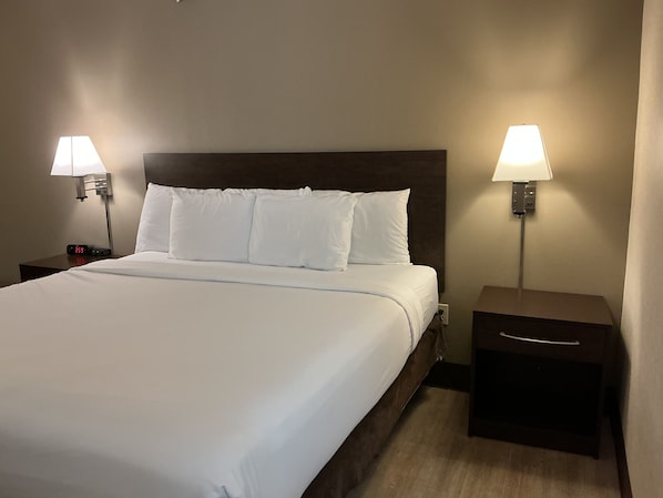 Una habitación de hotel con una cama grande, dos mesitas de noche y dos lámparas de pared.