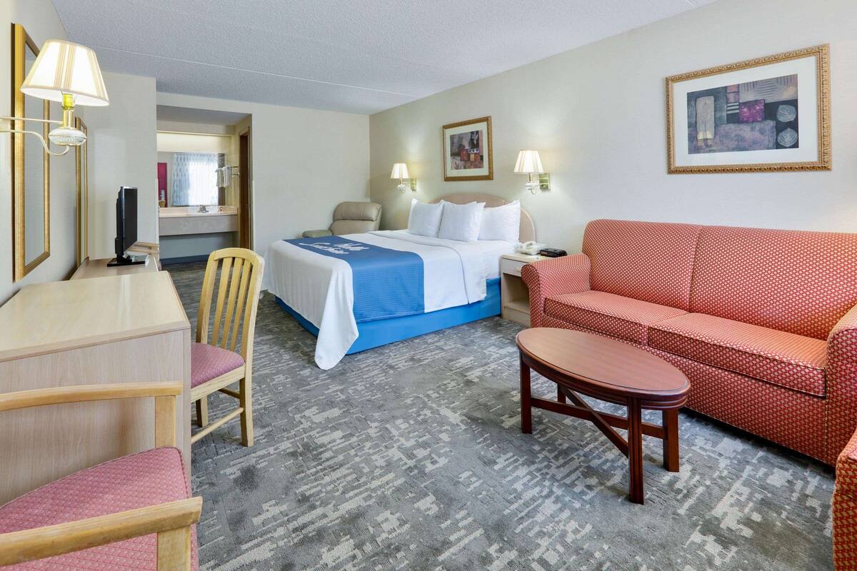 Hotelkamer met een bed, een rode bank, een houten stoel, een kleine tafel en een bureau met een lamp.
