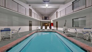 An indoor swimming pool with a clear view of the pool area, including the pool's edge, a few lounge chairs, and a door labeled 'R'.