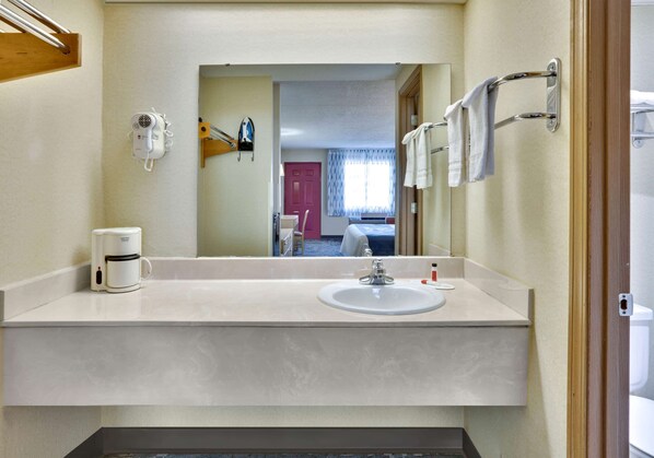 A bathroom with a sink, mirror, towel rack, and a coffee maker.