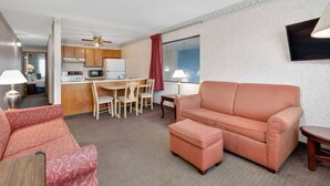 A hotel room with a kitchenette, a dining area, a sofa, and a TV mounted on the wall.