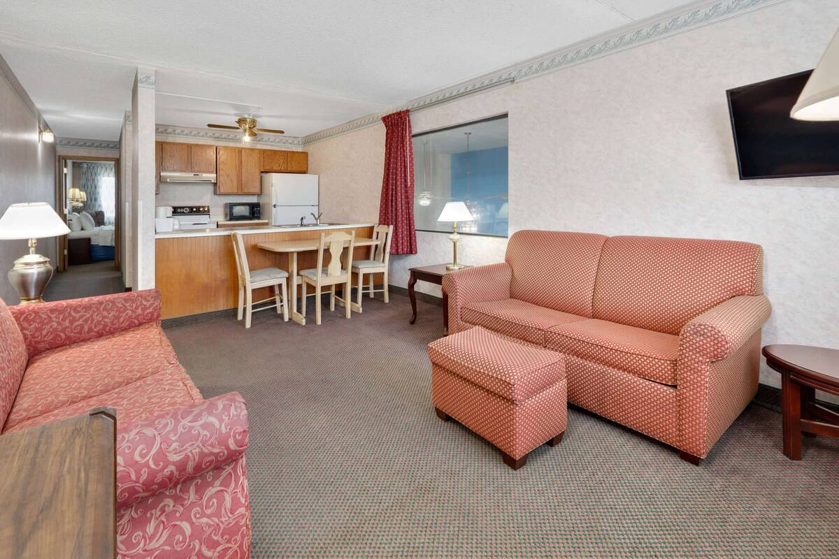 Een hotelkamer met een kitchenette, een eethoek, een bank en een aan de muur bevestigde televisie.