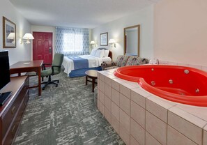 Een hotelkamer met een bed, een rode jacuzzi, een bureau met een televisie, een stoel, een klein tafeltje en een vloerbedekking.