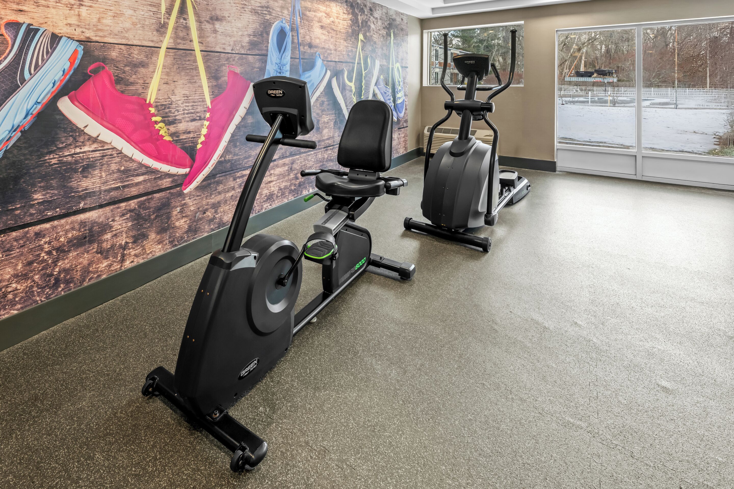 Un gimnasio con bicicletas estáticas, una caminadora y una pared decorada con obras de arte de zapatos.