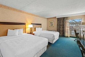 A hotel room with two beds, a desk, a chair, a lamp, a window with curtains, and a view of a building outside. - The Chelmsford Inn (Chelmsford)