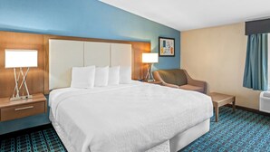 A hotel room with a large bed, two bedside tables with lamps, a chair, and a wall-mounted air conditioner.