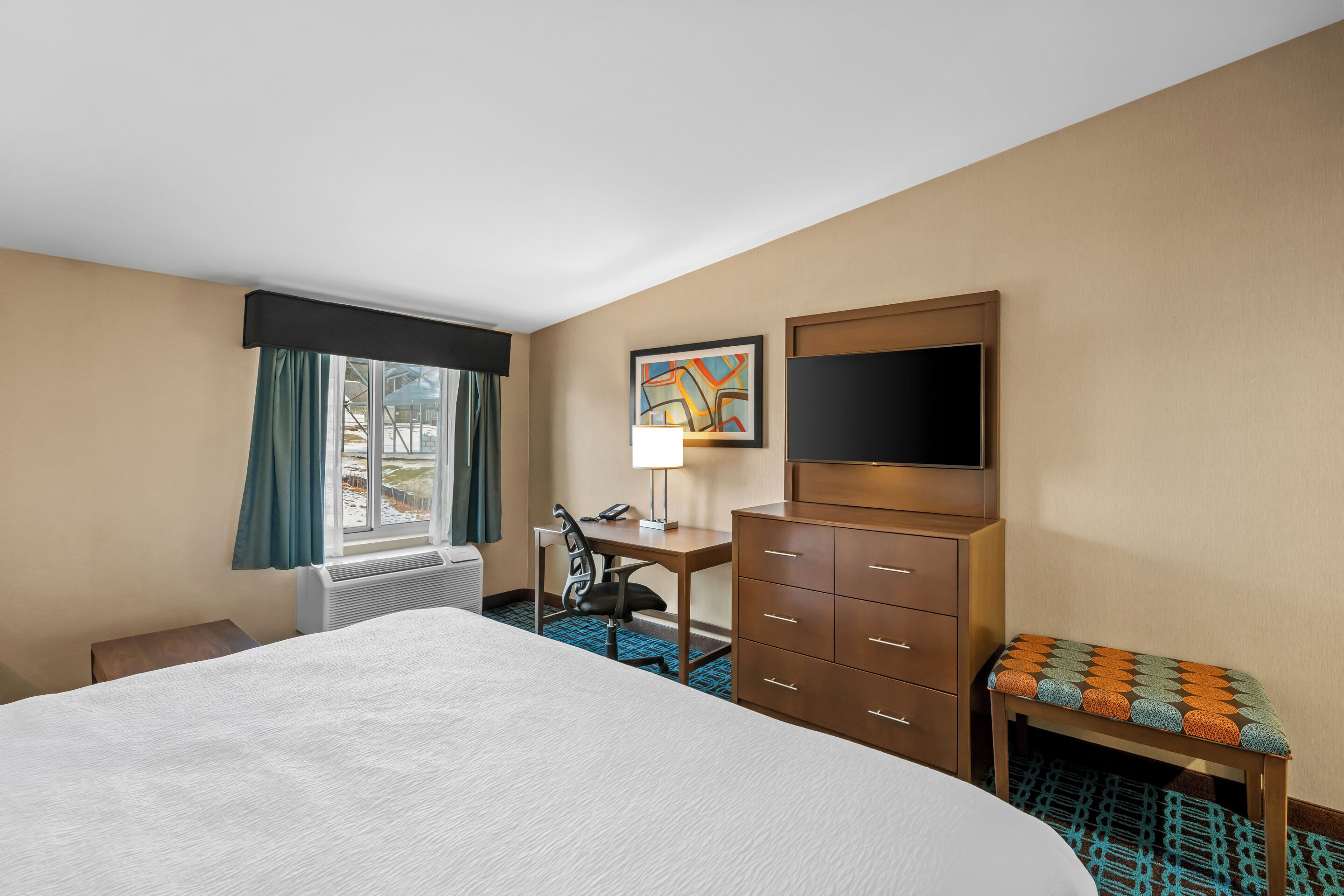 A hotel room with a bed, a desk, a chair, a television, and a window with curtains.