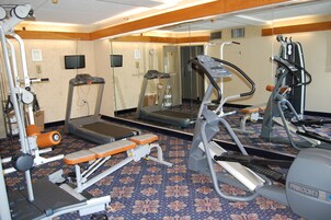 Un gimnasio con máquinas de cardio, equipo de entrenamiento de fuerza y un espejo grande.