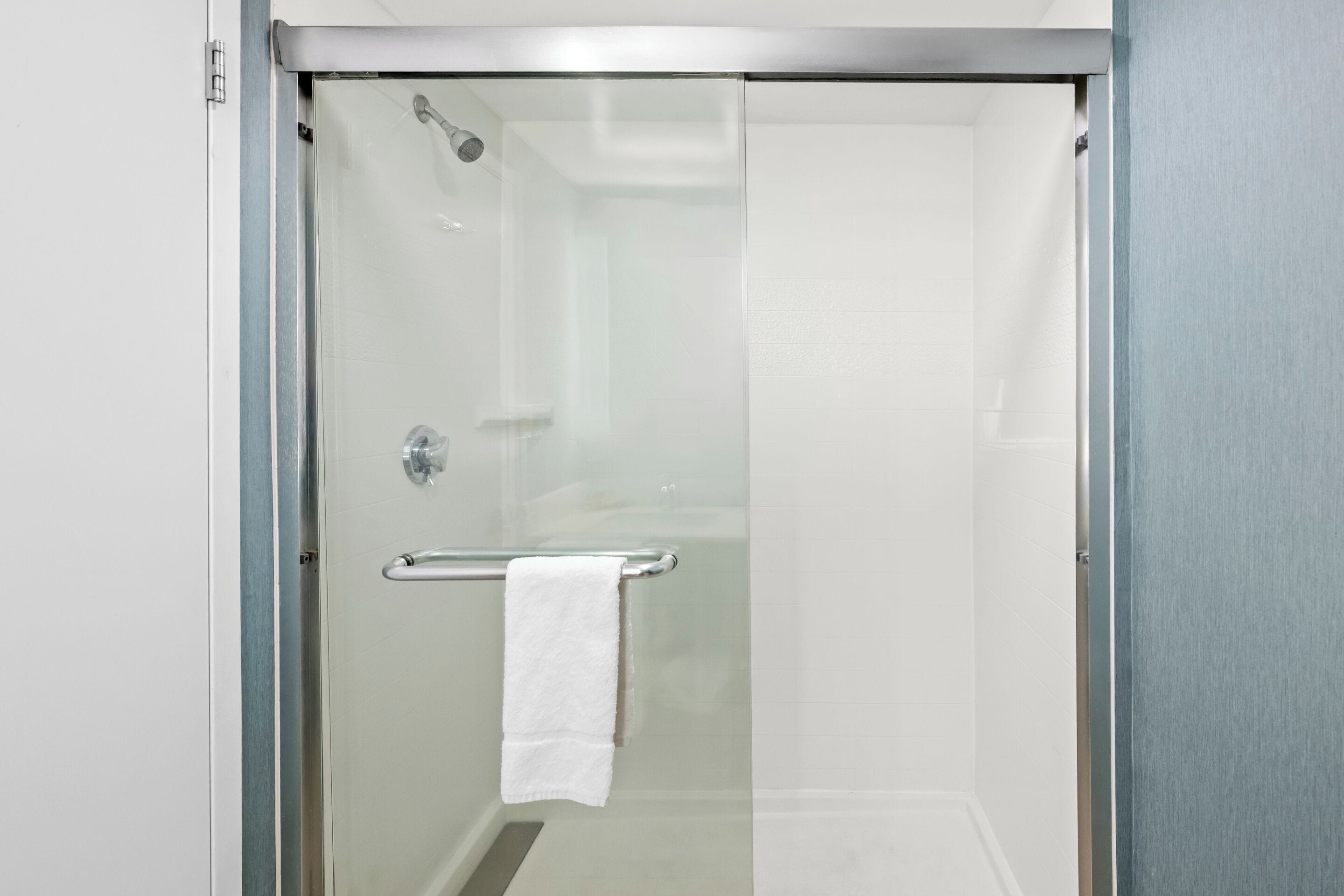 Cabina de ducha con paredes de vidrio y una toalla blanca sobre una barra metálica.