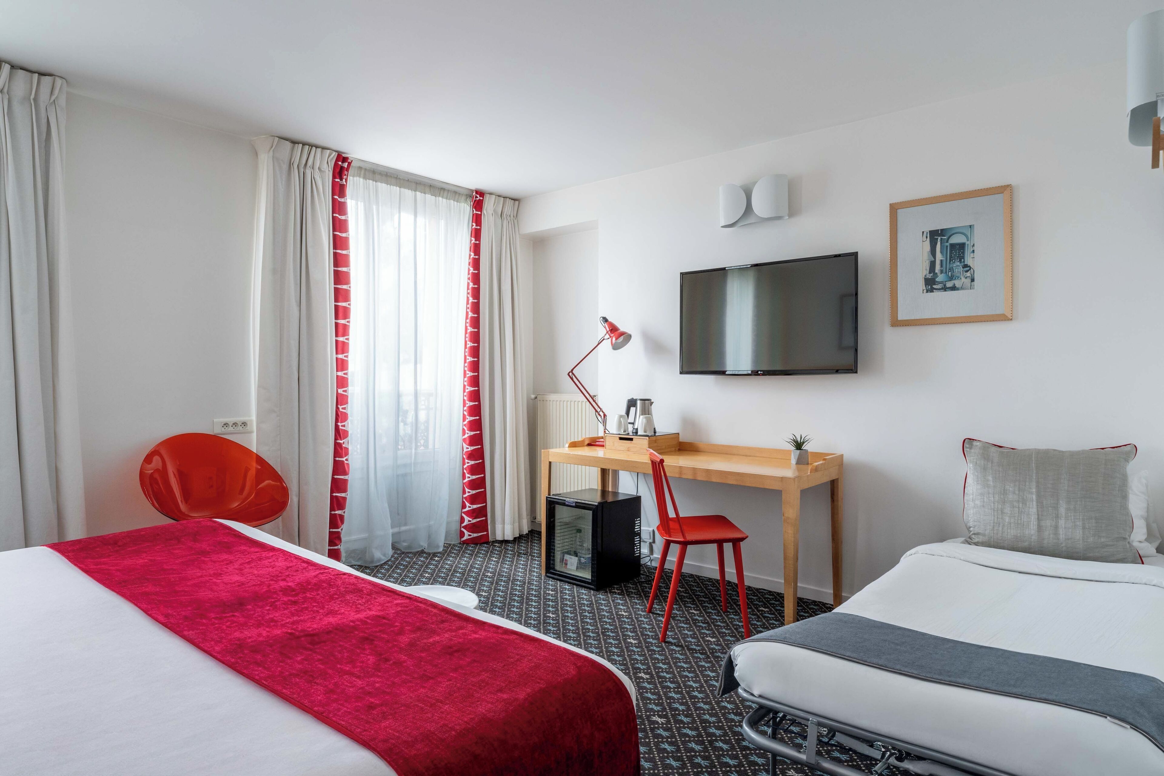 A hotel room with two beds, a desk, a chair, a television, and a small table.