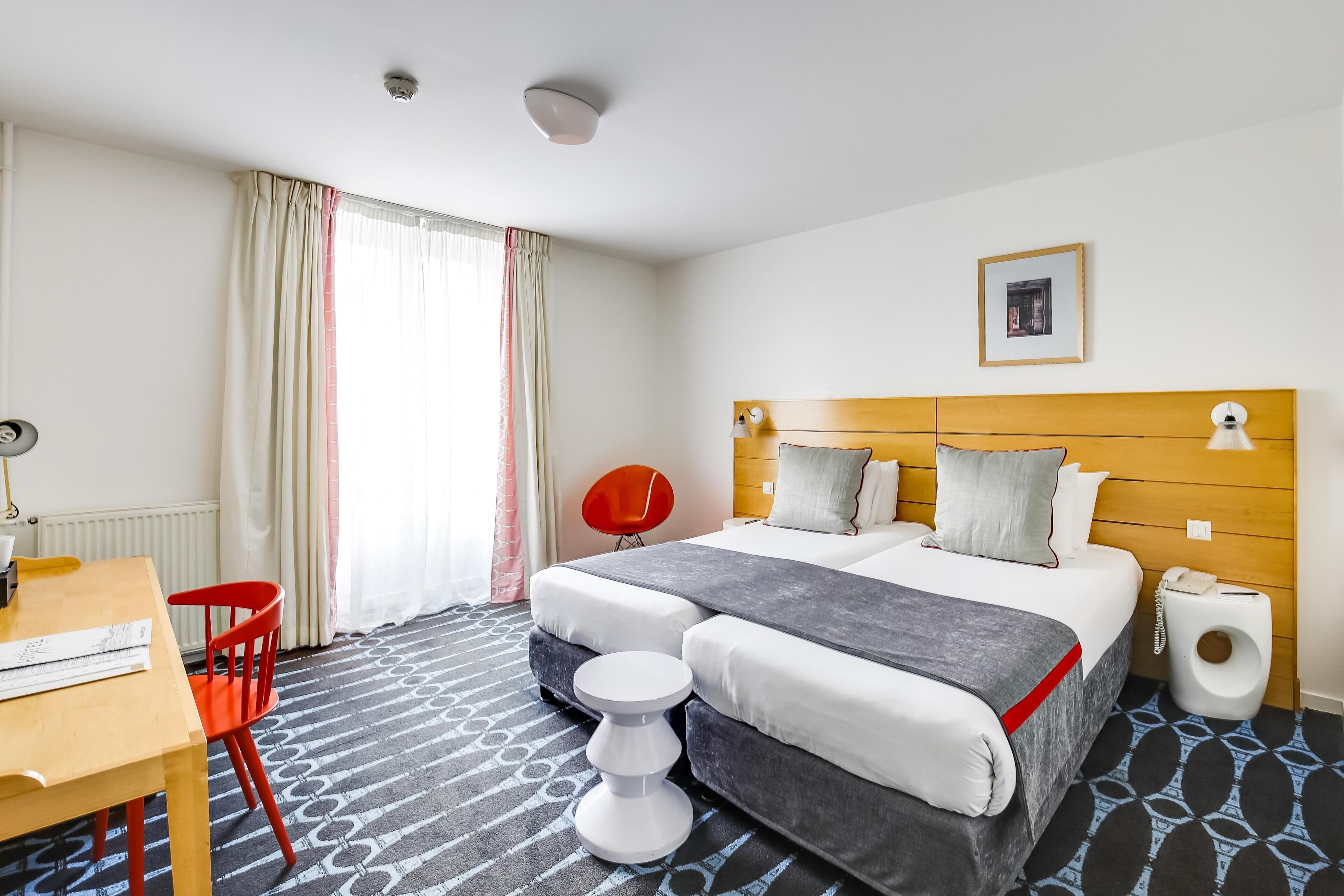 Ein Hotelzimmer mit Bett, Schreibtisch, Stuhl, Nachttisch und einem Fenster mit Vorhängen.