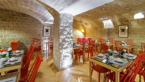 A restaurant with stone walls, wooden tables, and red chairs. - Hôtel Lorette - Astotel (Paris)