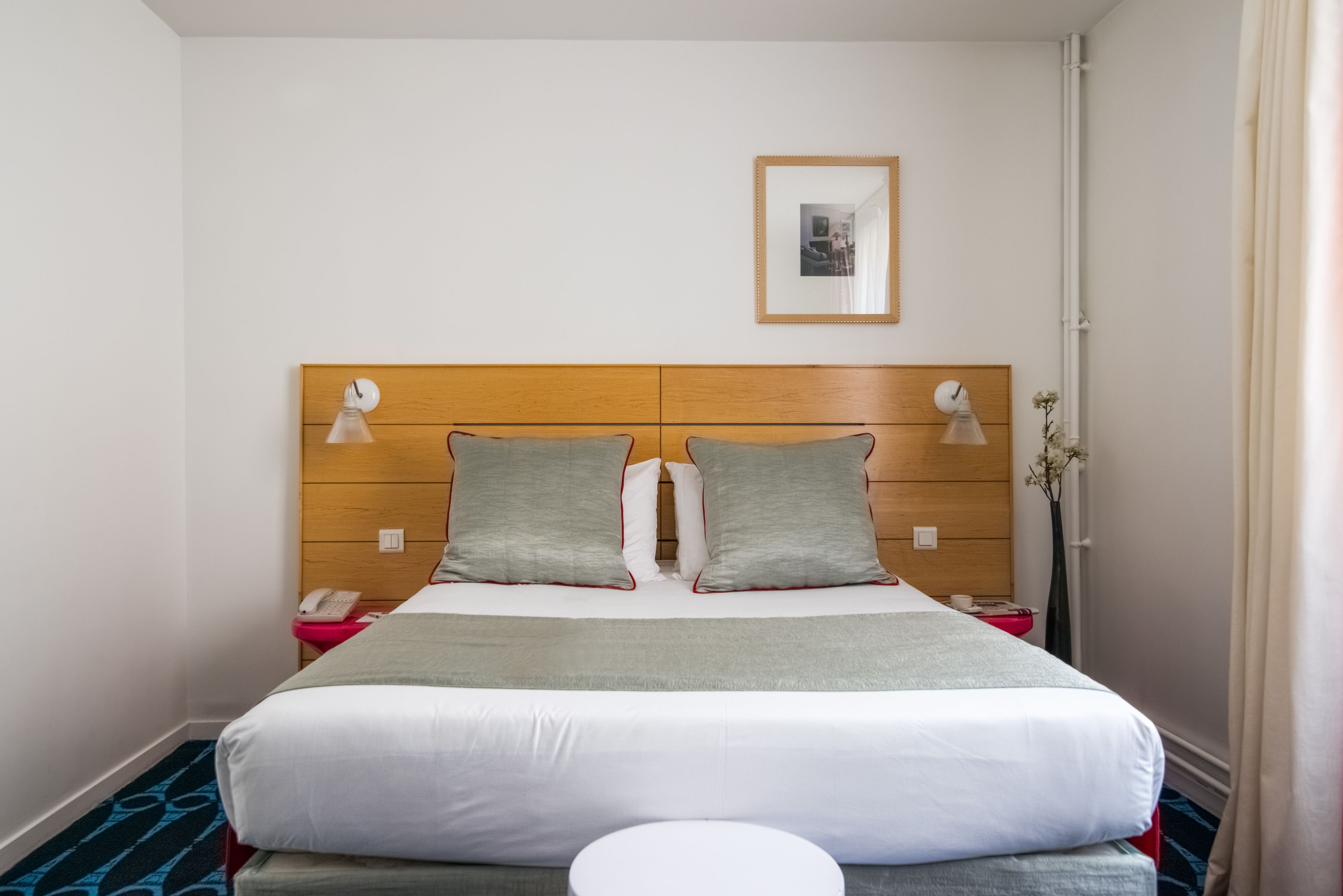 A neatly made bed with a wooden headboard, two bedside lamps, a bedside phone, and a small table with a vase of flowers.