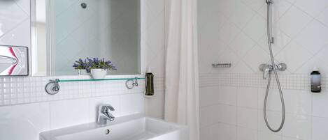 A bathroom with a white sink, a glass shelf with flowers, a shower with a handheld showerhead, and a mirror.