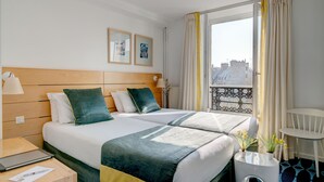 A hotel room with two beds, a desk with a laptop, a small table with a speaker, and a window with curtains. - Hôtel Lorette - Astotel (Paris)