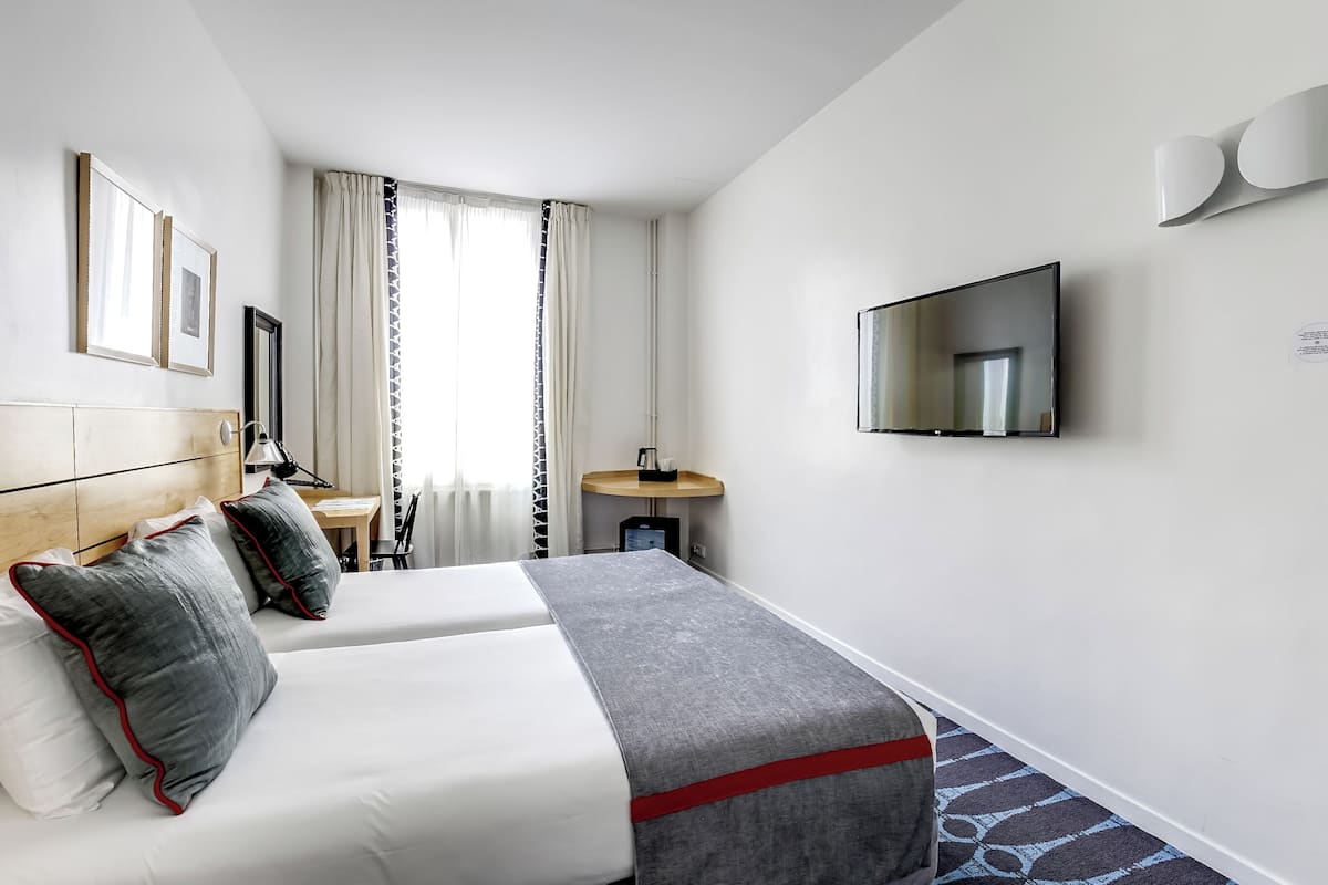 Habitación de hotel con dos camas, televisión, escritorio y ventana con cortinas.