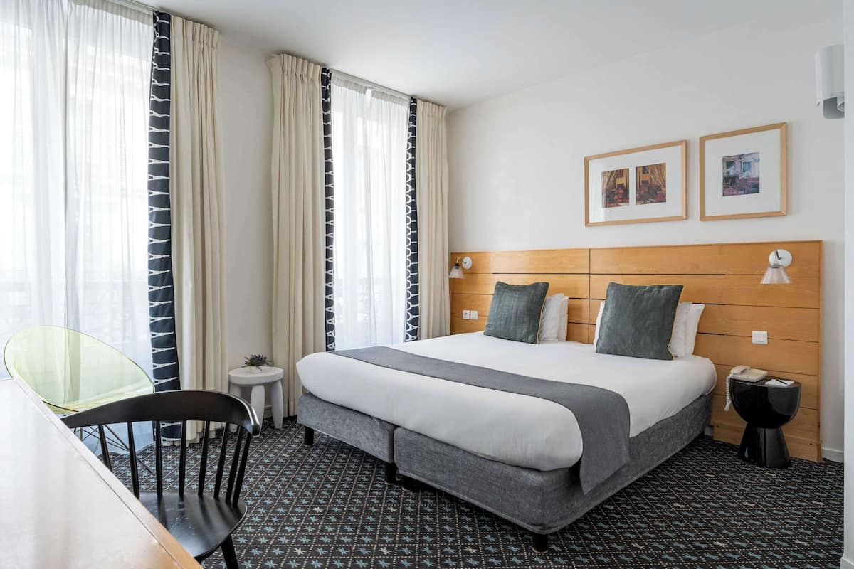 Una habitación de hotel con una cama grande, una mesita de noche pequeña, una silla y un escritorio.