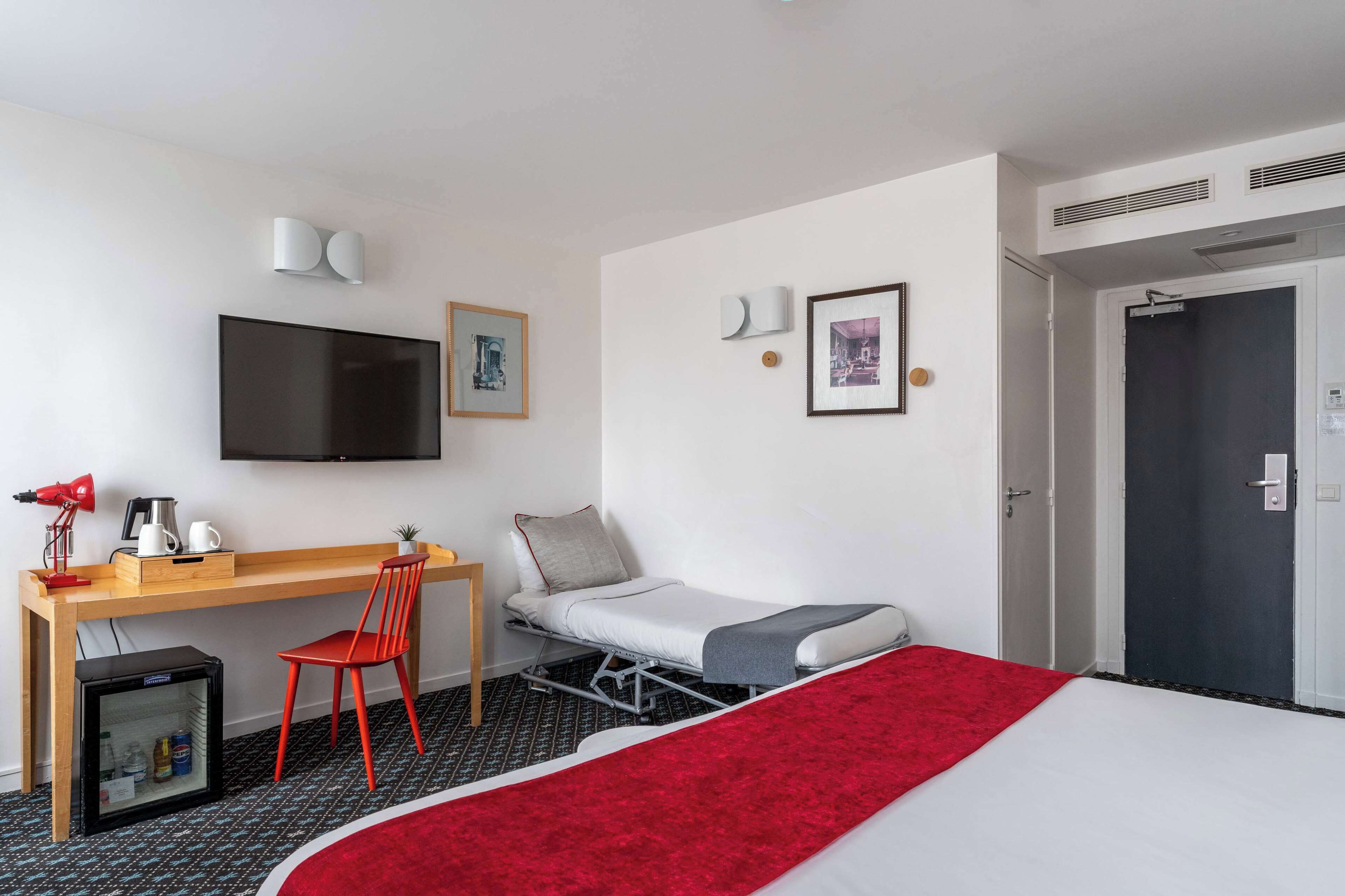 Una habitación de hotel con una cama, un escritorio, una silla, un televisor y una puerta.