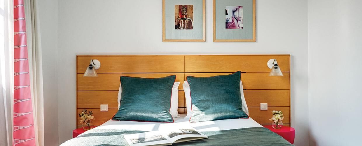 A bed with a wooden headboard, two pillows, a bedside table, and two wall-mounted lamps.
