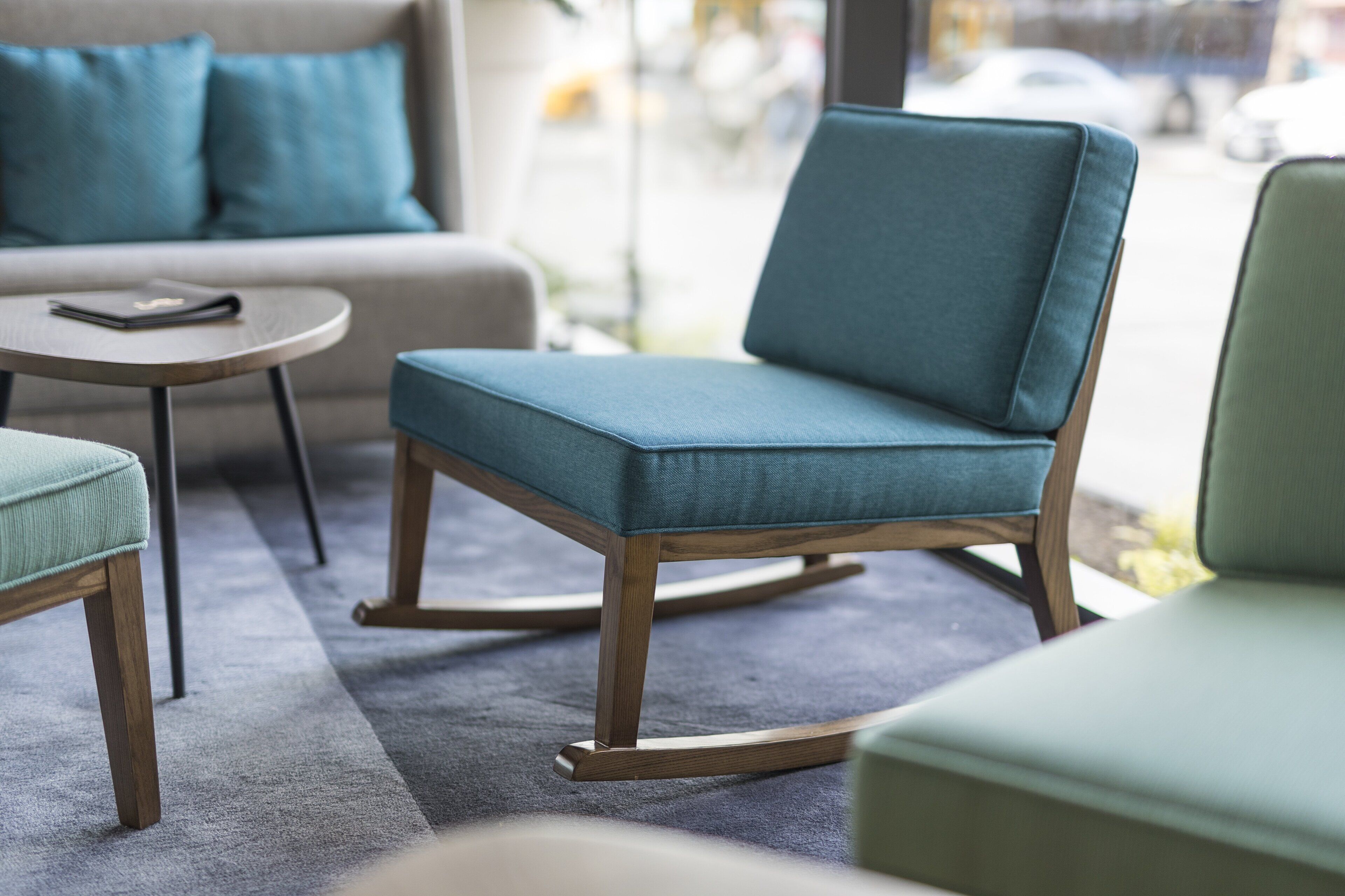 Un salon moderne avec un fauteuil turquoise, une petite table ronde et un canapé.