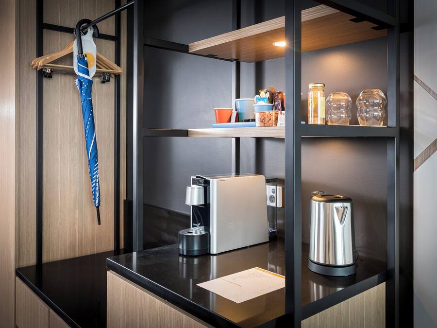 A modern kitchen with a coffee machine, kettle, and storage shelves.