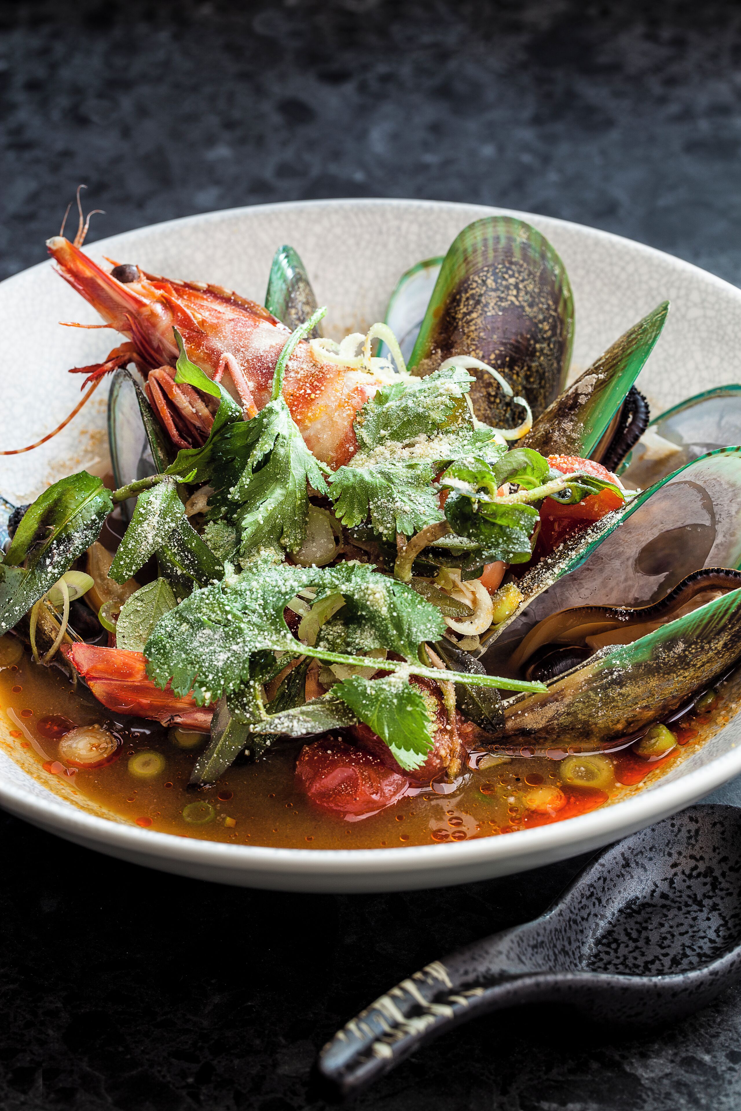 A bowl of seafood soup with mussels and shrimp, garnished with herbs and lemon slices.