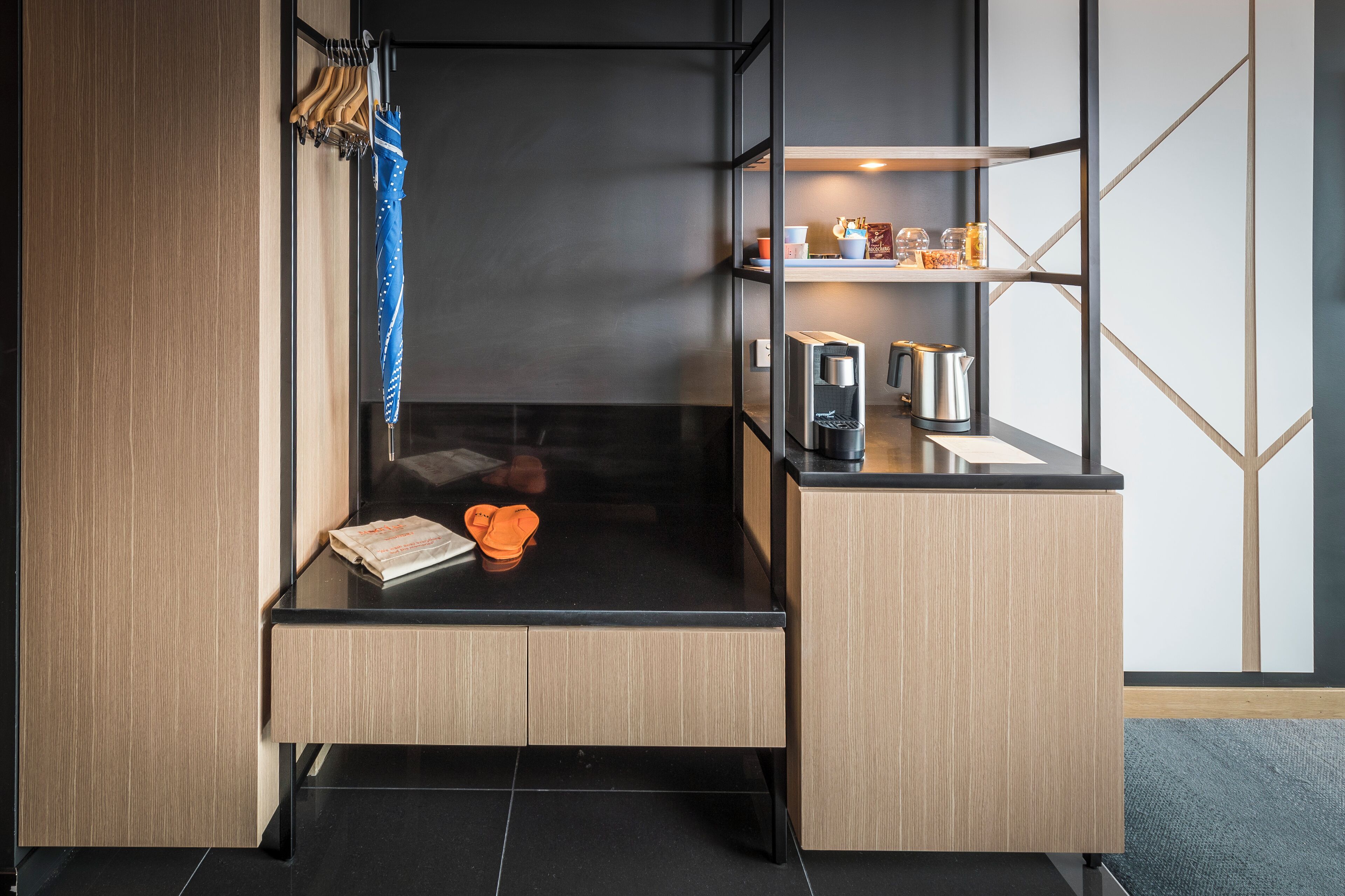 Une chambre d’hôtel moderne dotée d’une paroi en verre, d’une petite kitchenette, d’une étagère avec des articles de toilette et d’un coin salon bien aménagé.