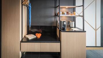 Une chambre d’hôtel moderne dotée d’une paroi en verre, d’une petite kitchenette, d’une étagère avec des articles de toilette et d’un coin salon bien aménagé.
