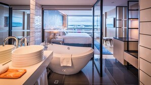 A modern bathroom with a large bathtub, a sink, and a mirror. There is a view of a balcony with a cityscape in the background. - M Social Hotel Auckland (Auckland)