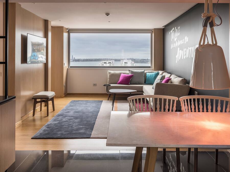 Una sala de estar moderna con un ventanal grande, un sofá, una mesa de comedor y una zona de cocina.