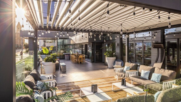 An outdoor seating area with modern furniture, a glass wall, and a ceiling with hanging lights. - M Social Hotel Auckland (Auckland)