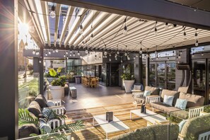 An outdoor seating area with modern furniture, a glass wall, and a ceiling with hanging lights.