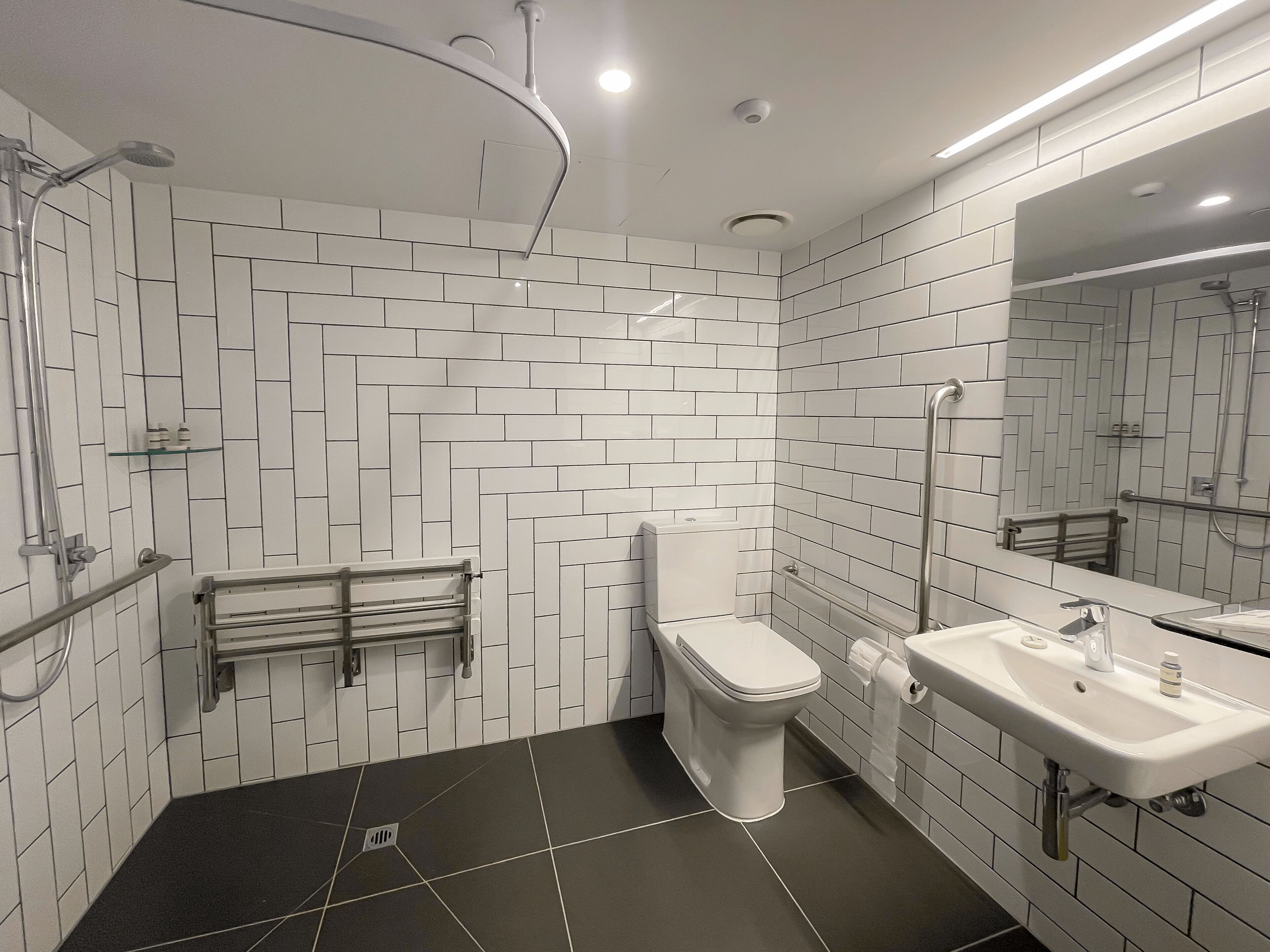 Casa de banho moderna com azulejos brancos em padrão herringbone, chão em mosaico preto, sanita, lavatório e zona de duche.
