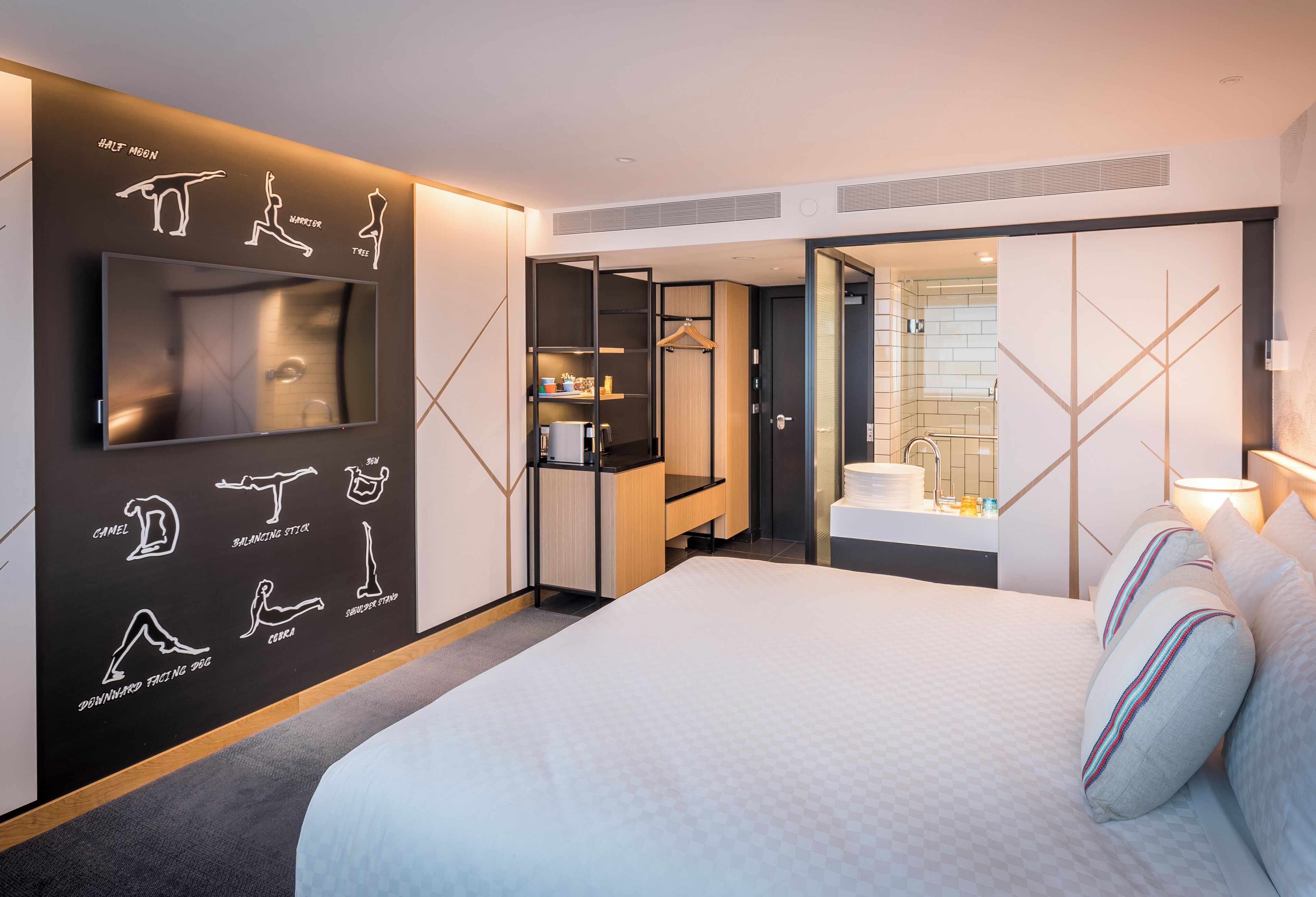 A hotel room with a bed, a TV, a wardrobe, a bathroom, and a wall with exercise illustrations.