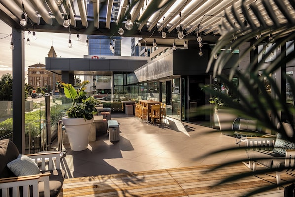 Une terrasse extérieure moderne, aménagée avec des sièges, des plantes en pot et des luminaires suspendus.