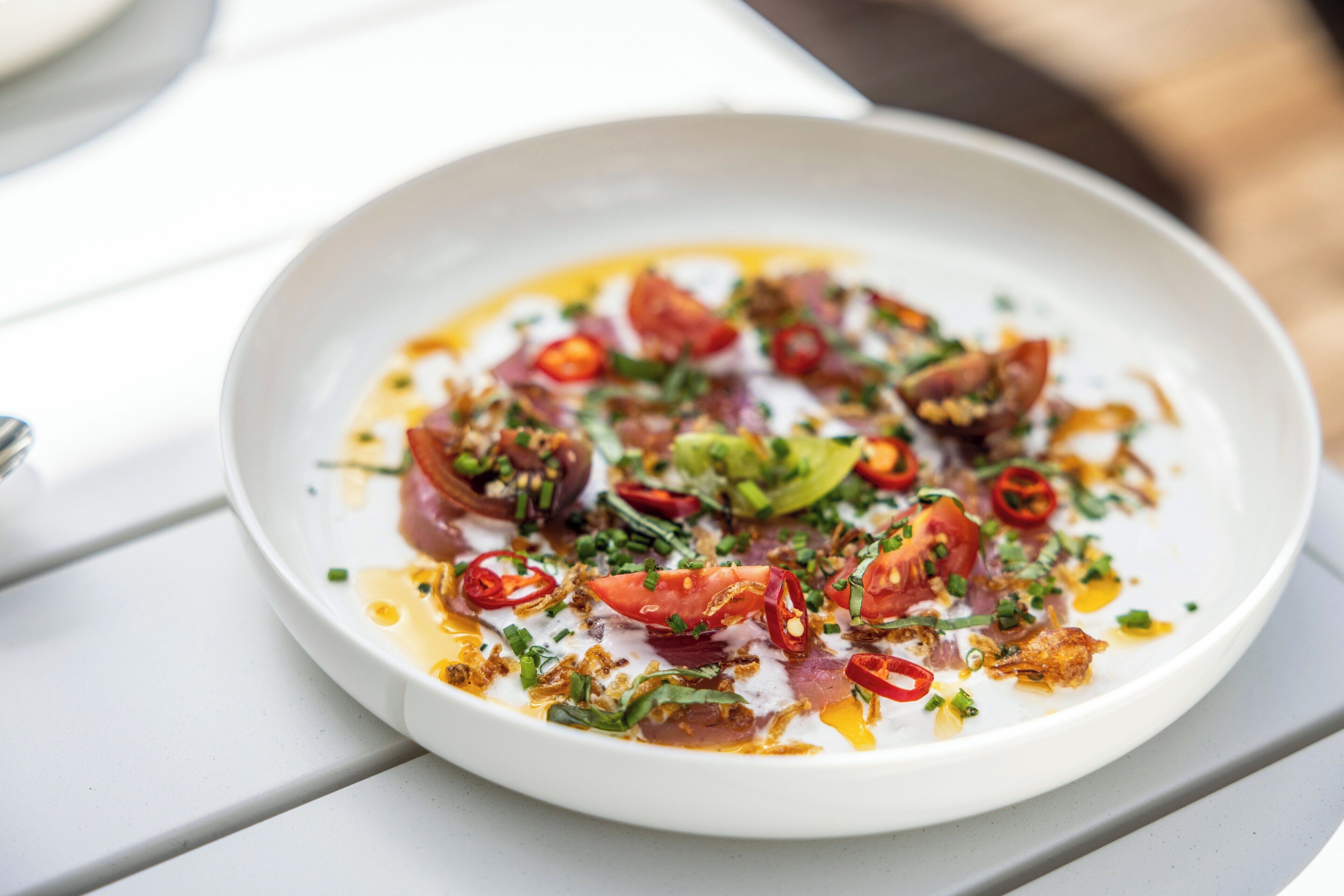 A white plate with a dish of food, garnished with herbs and red chili slices.