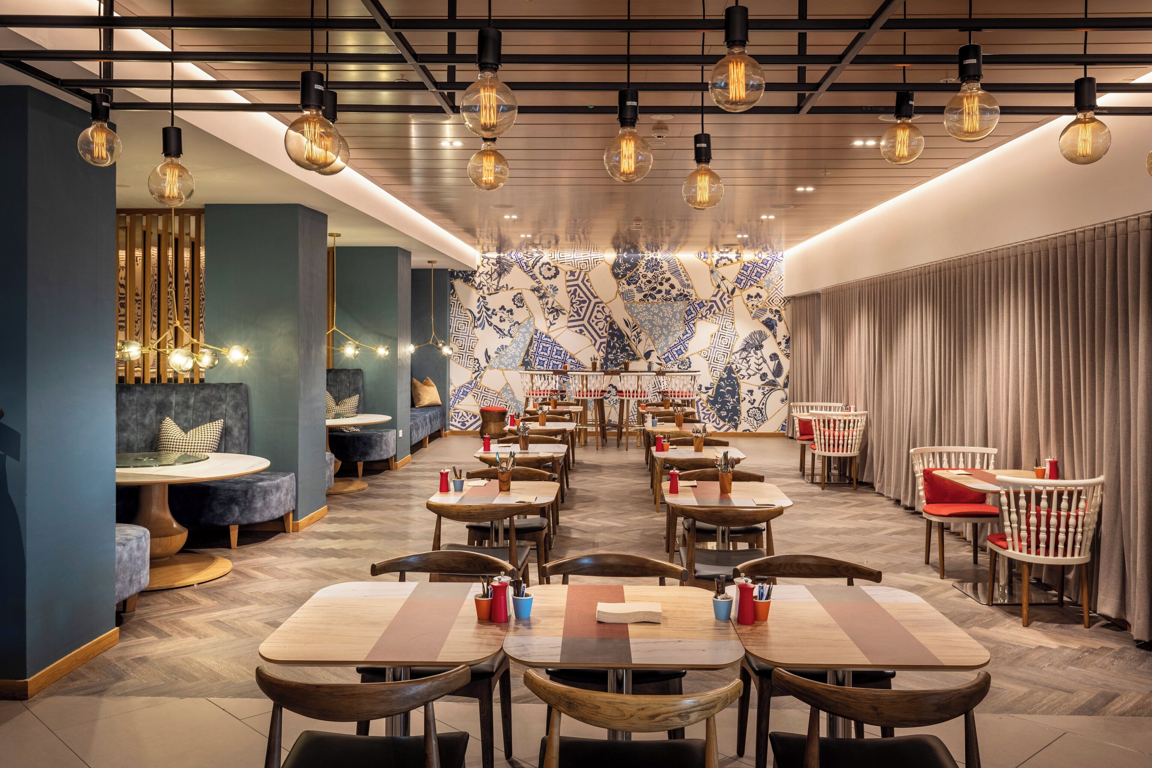 Un restaurante con varias mesas y sillas, un papel tapiz decorativo y lámparas colgantes.