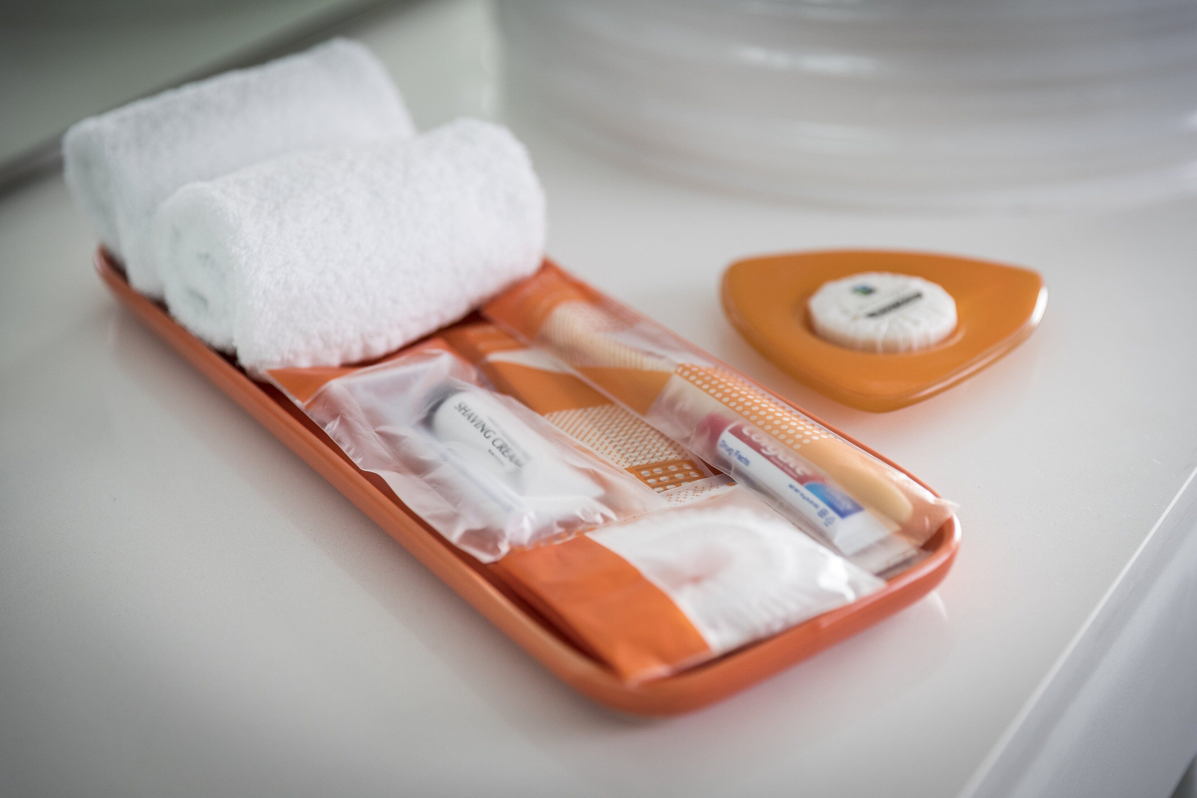 A bathroom with a white sink, a towel rack with two white towels, a toothbrush, a razor, and a soap dish.