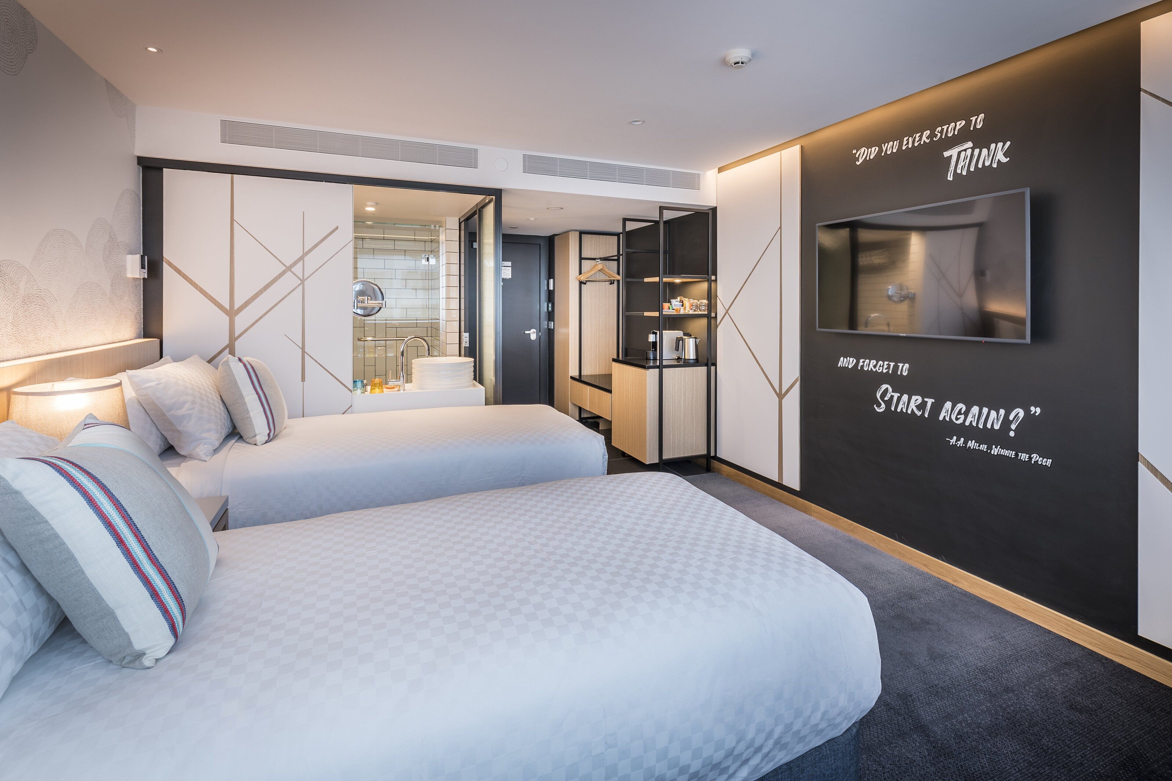 Et moderne hotelværelse med en stor seng, et fjernsyn ophængt på væggen og et motiverende citat.