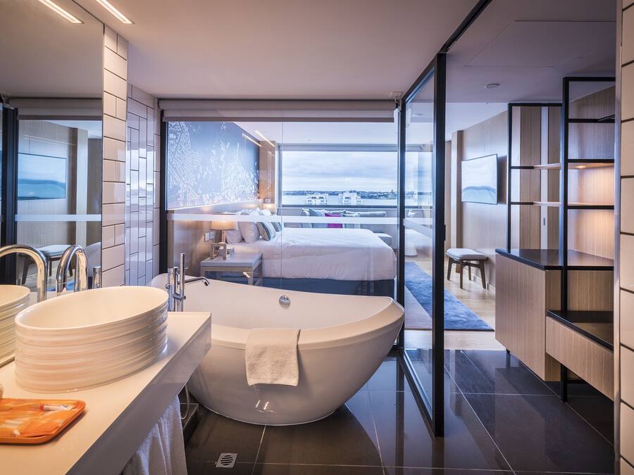 Un baño moderno con una bañera grande, un lavabo y un espejo. Se ve una habitación con una cama y un balcón.