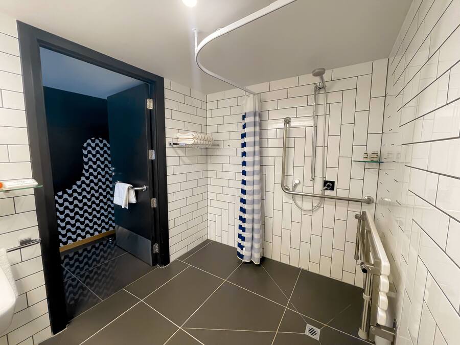 A modern bathroom with white tiled walls, a shower with a glass door, and a towel rack.