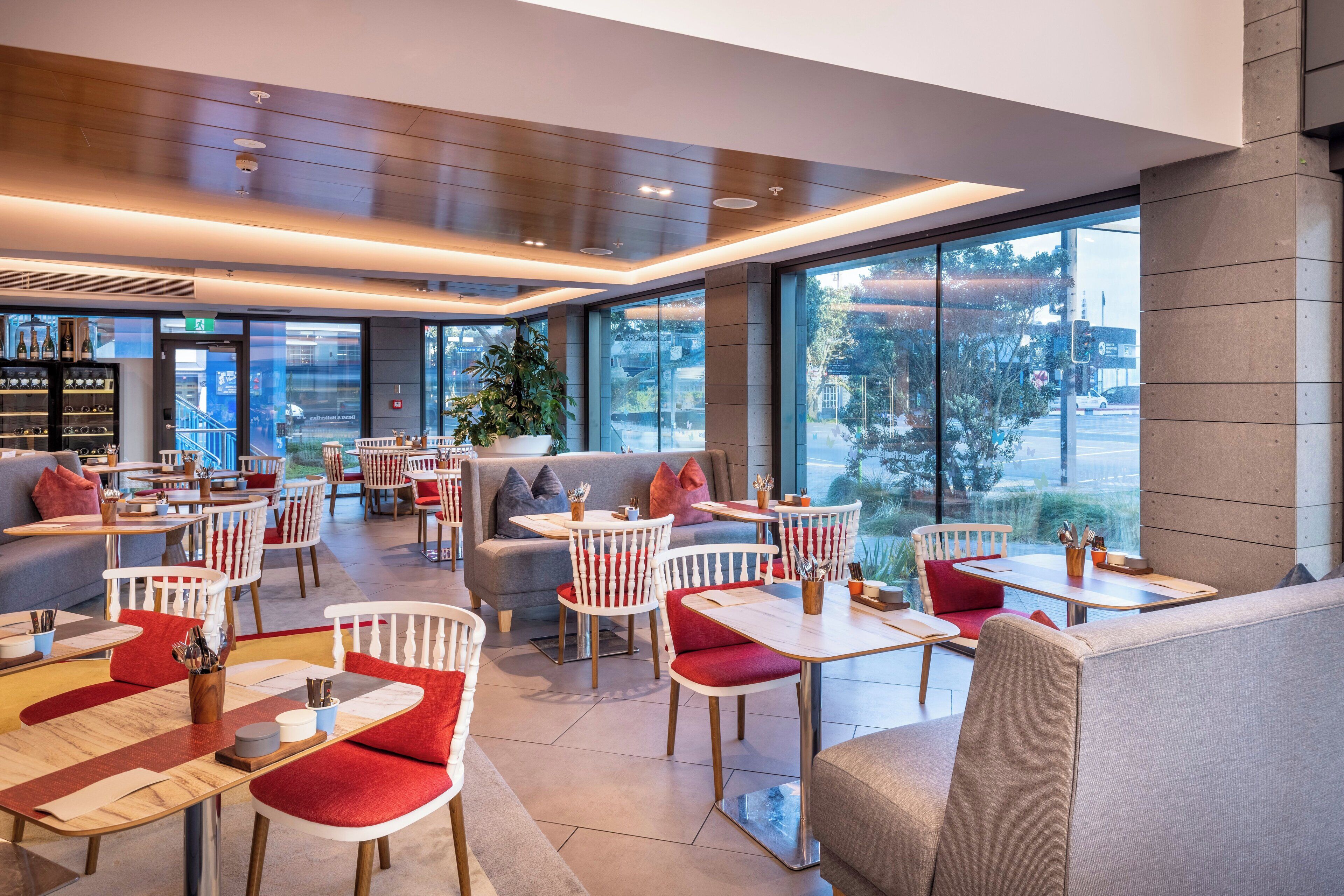 Ein modernes Restaurant mit hohen Decken, großen Fenstern und verschiedenen Sitzgelegenheiten, darunter Tische und gemütliche Nischen.